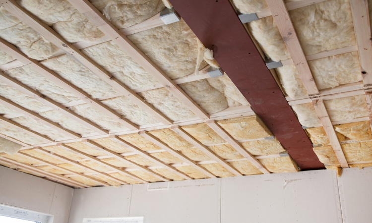 Isolation de plafond en laine minérale posée entre les solives d'une ossature bois en cours de chantier